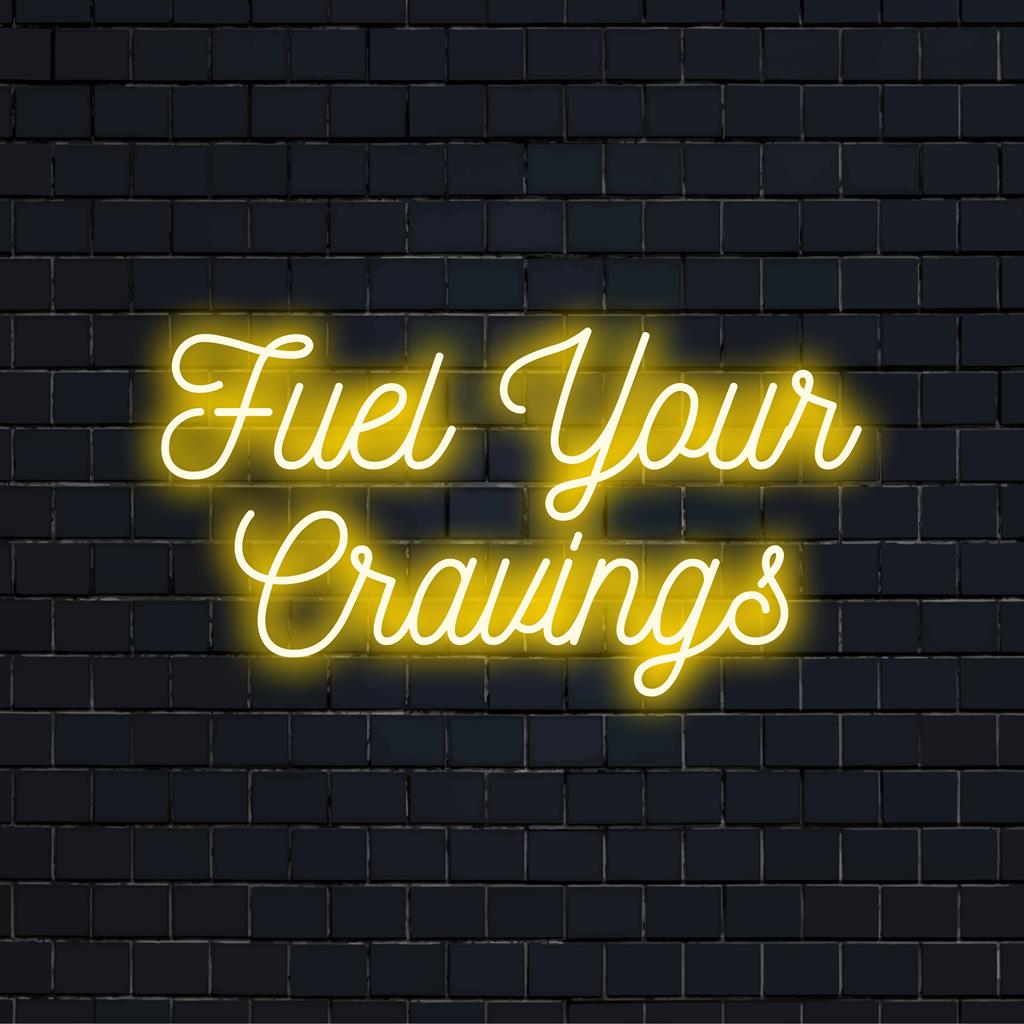 Anpassad LED-neonskylt med frasen Fuel Your Cravings, med modern typografisk design och livfulla neonfärger.