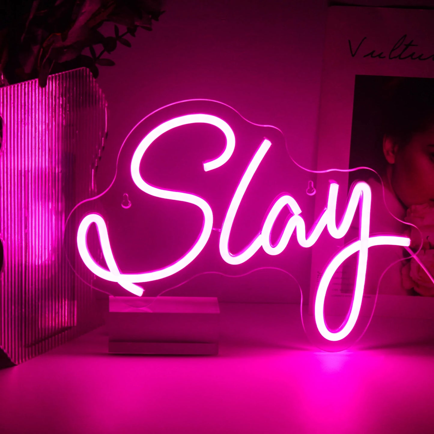 Bilden har en levande, handgjord LED-neonskylt som visar ordet "Slay" i ett elegant, kursivt teckensnitt.