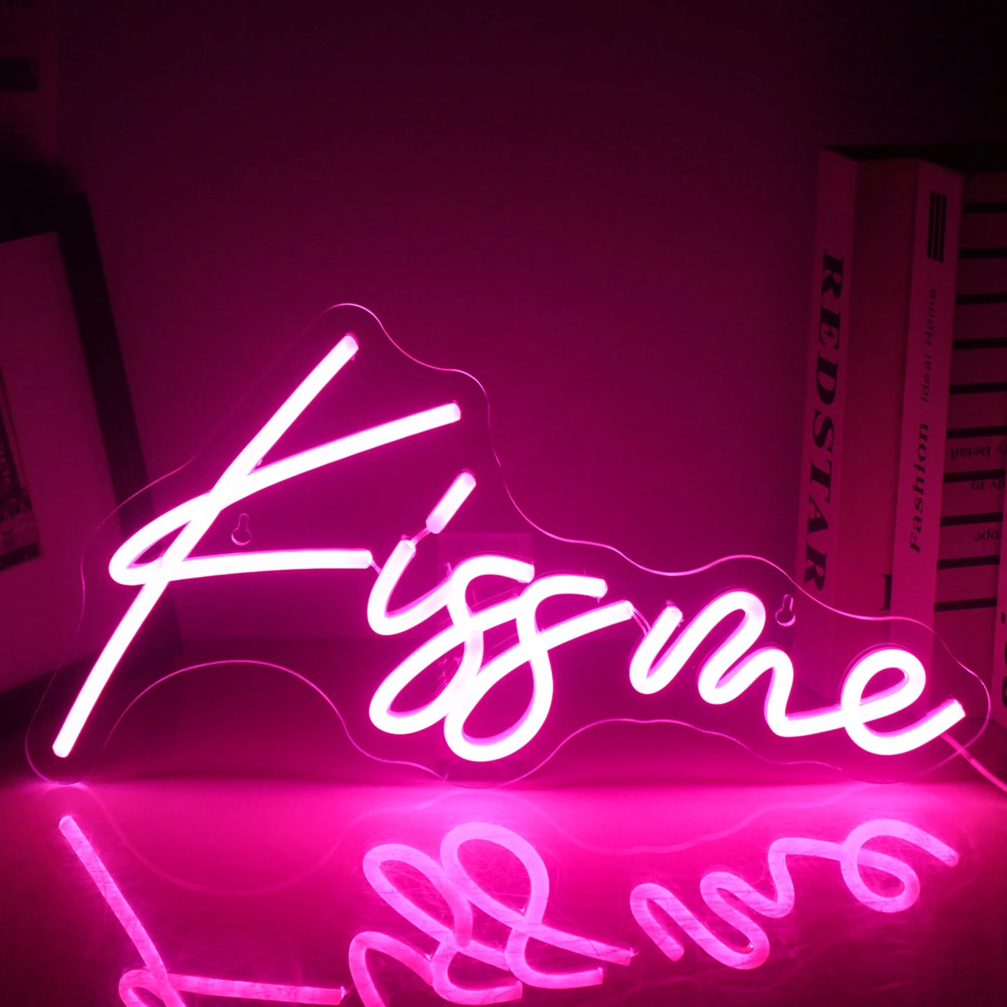 En livlig "Kiss Me" LED neonskylt är upplyst och visar ljusa och djärva rosa bokstäver mot en mörk bakgrund.