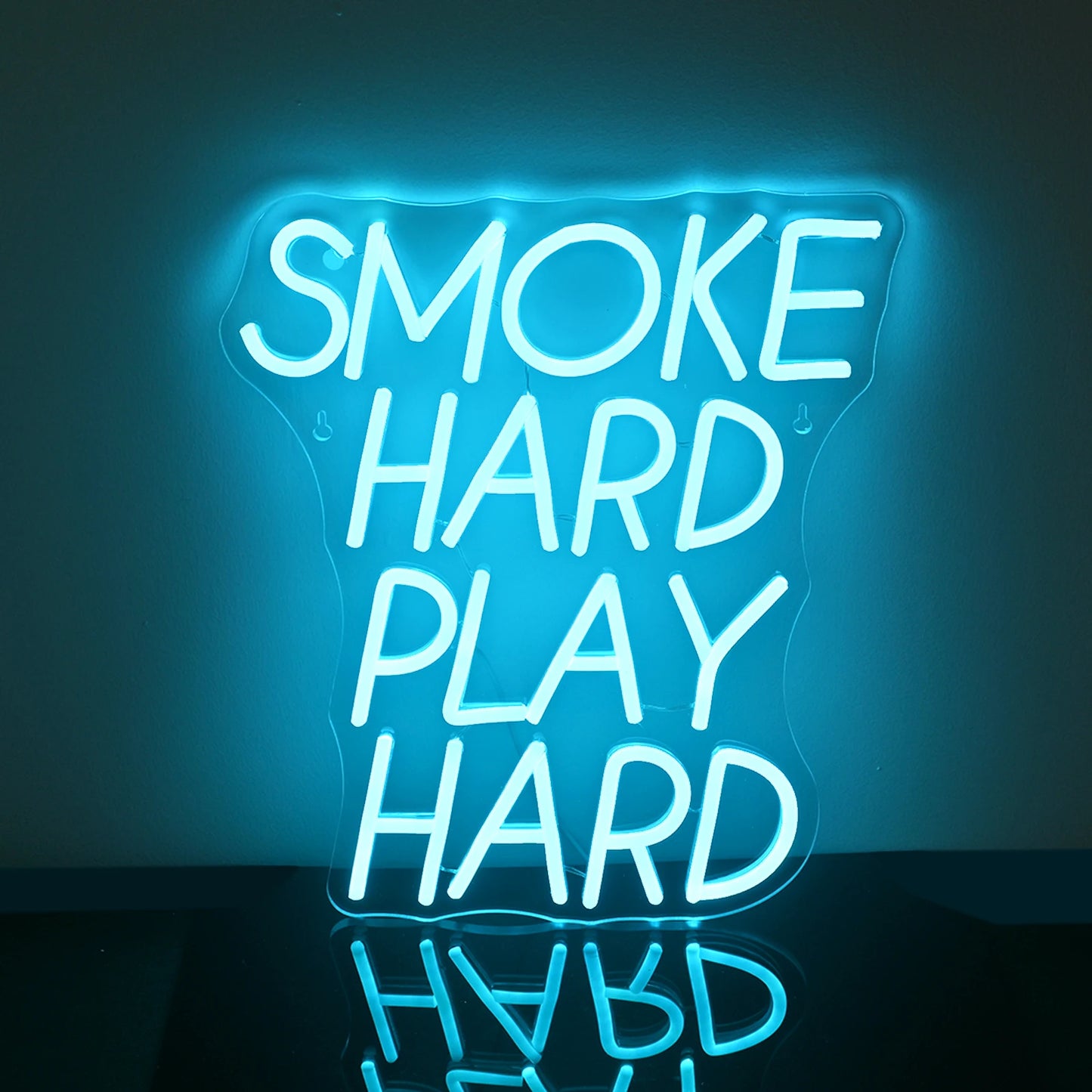 Bilden visar en levande LED-neonskylt som läser "Smoke Hard Play Hard" i fetstil, versaler.