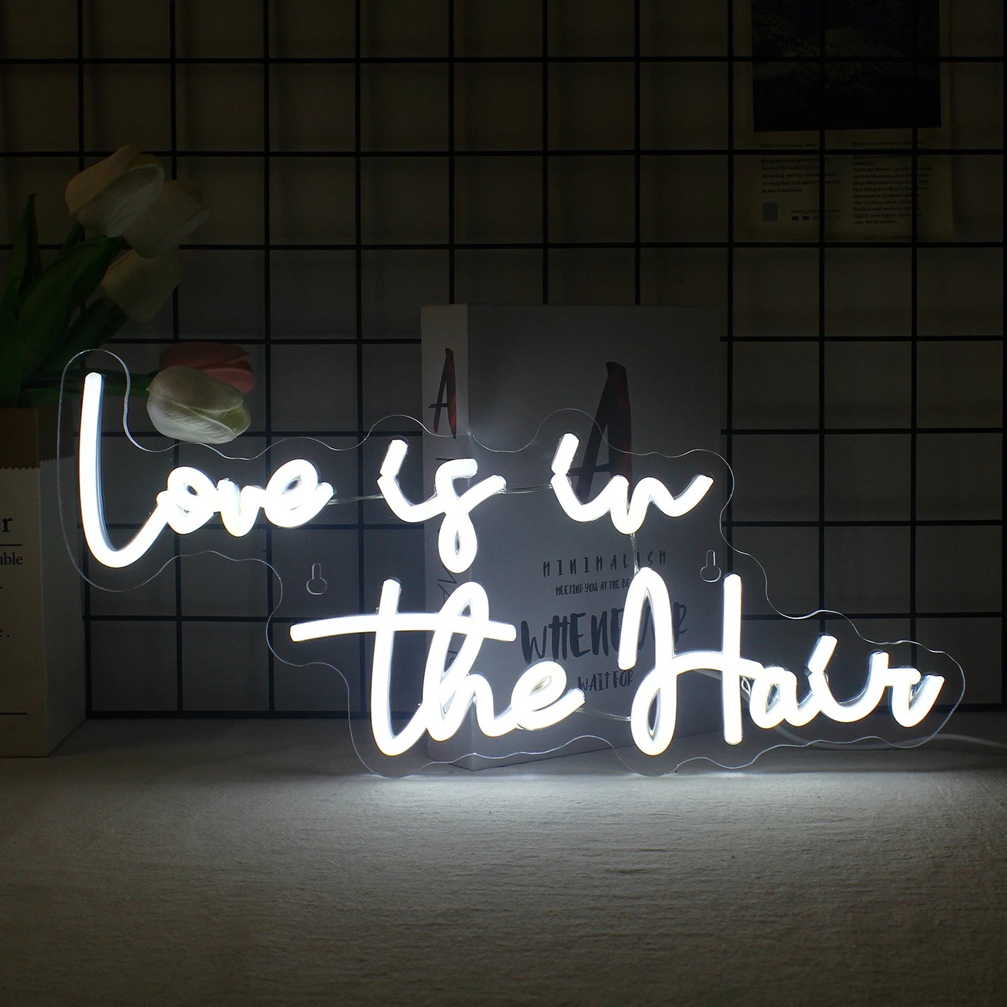 Bilden visar en levande LED-neonskylt som stavar frasen "Love is in the Hair" i stilfullt, flytande manus.