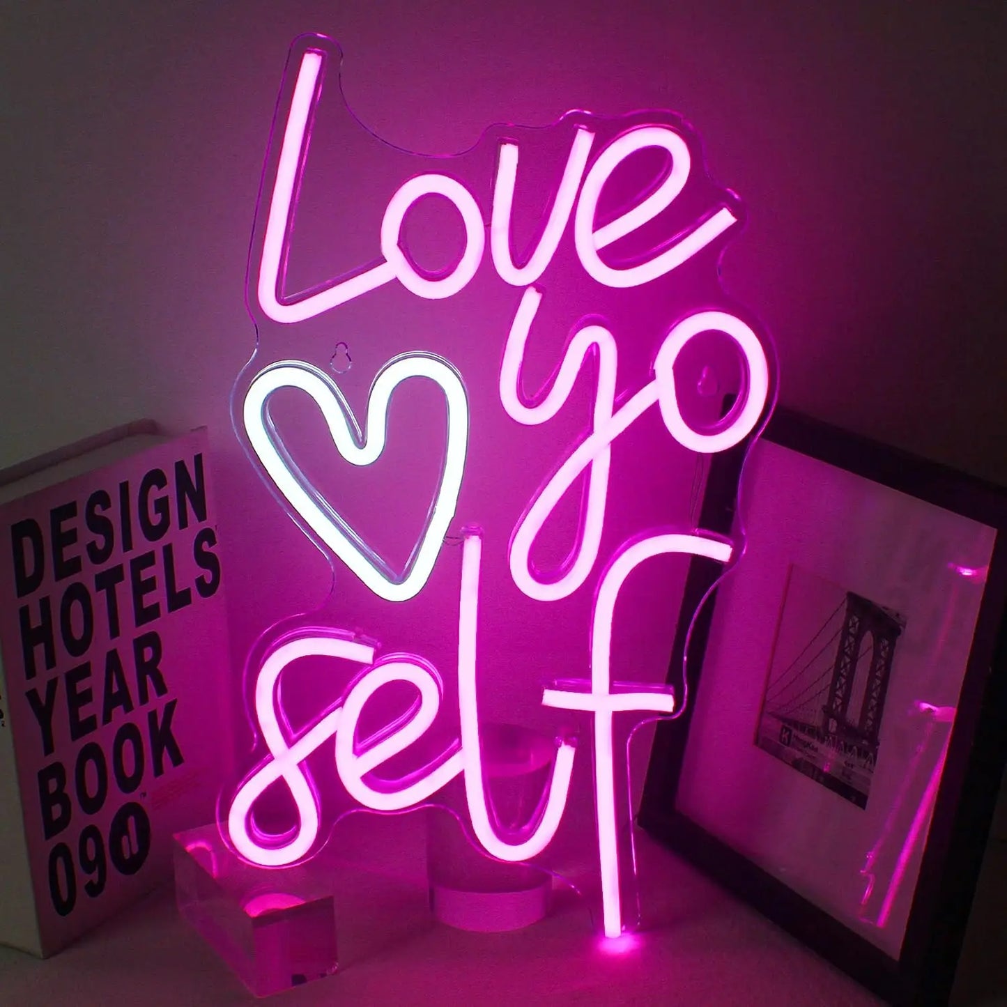 En livlig "Love Yo Self" LED neonskylt visas mot en enkel, mörk bakgrund.
