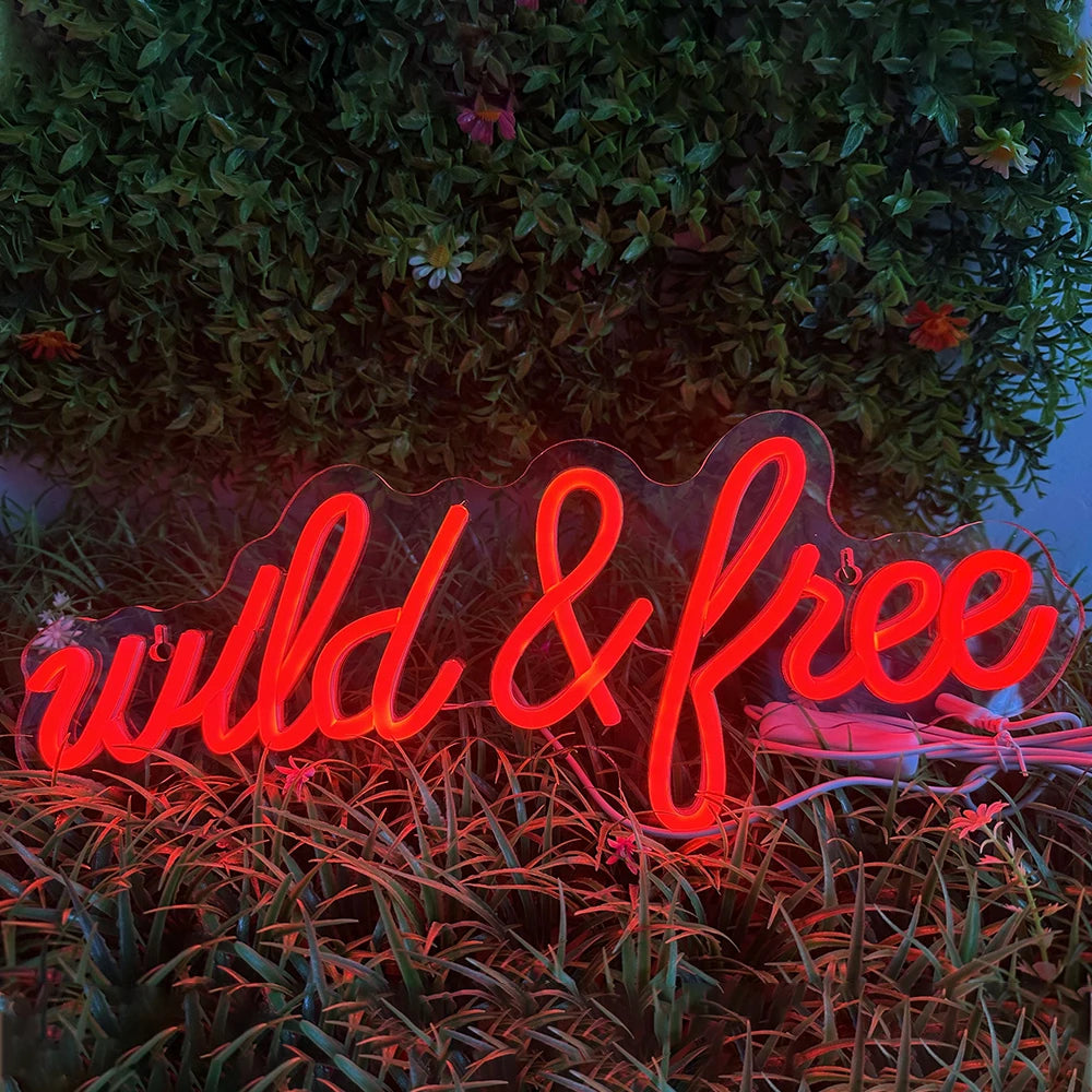 Bilden har en levande LED-neonskylt som visar orden "Wild & Free" i ett elegant, kursivt teckensnitt.