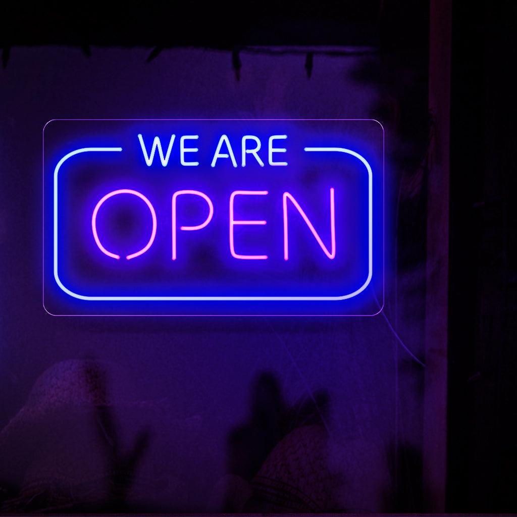 En fängslande neonskylt som stolt visar orden "We are Open" i fetstilta, lysande bokstäver, vilket signalerar att ett företag är redo och tillgängligt för att betjäna sina kunder.
