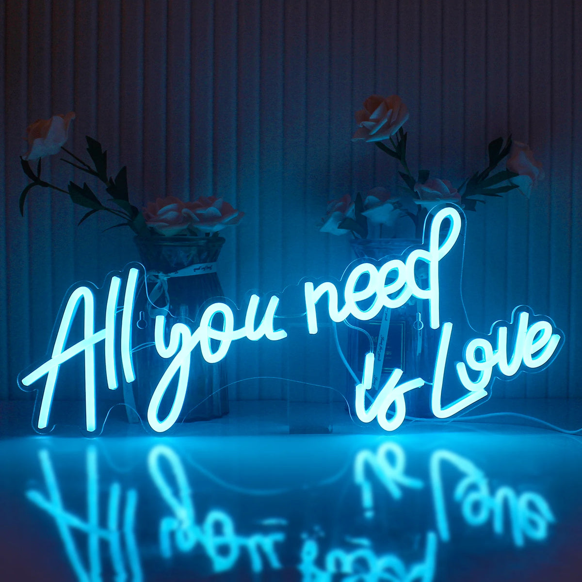 Bilden visar en levande LED-neonskylt som stavar ut frasen "All You Need Is Love" i ett elegant, kursivt teckensnitt.