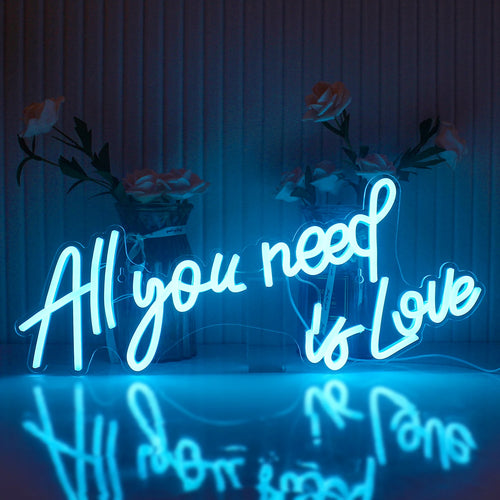 Bilden visar en levande LED-neonskylt som stavar ut frasen "All You Need Is Love" i ett elegant, kursivt teckensnitt.