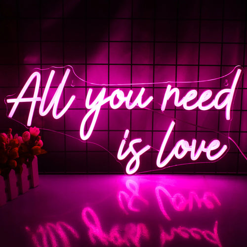 Bilden visar en levande LED-neonskylt med frasen "All You Need is Love" med eleganta, kursiva bokstäver.