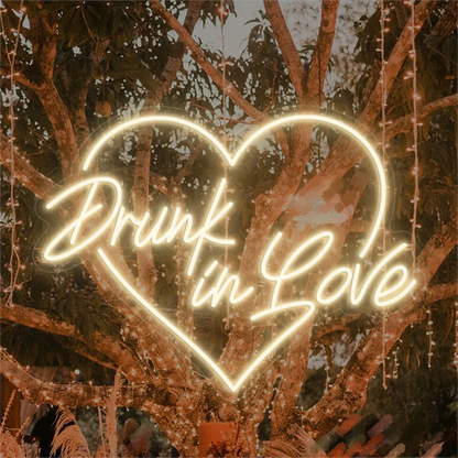 The image features a stylish LED neon sign that spells out the phrase "Drunk in Love" in a vibrant, glowing cursive font.