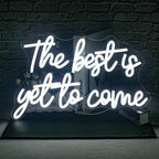 Bilden visar en levande, handgjord LED-neonskylt som läser "The Best is Yet to Come" i ett elegant, kursivt teckensnitt.
