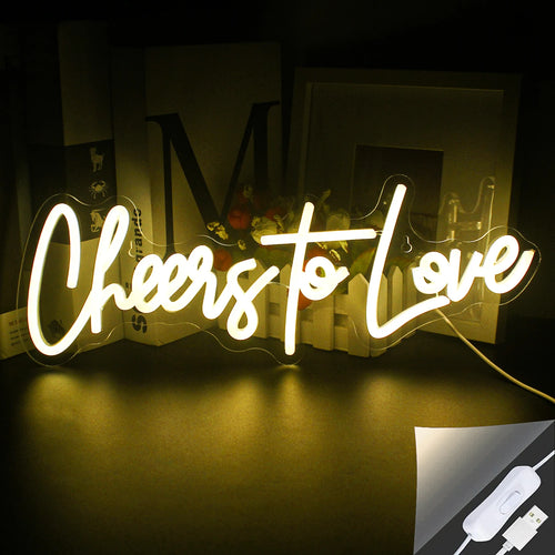 Bilden visar en levande, handgjord LED-neonskylt som stavar ut "Cheers to Love" i ett stilfullt skripttypsnitt.
