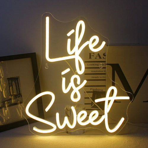 Bilden har en levande, handgjord LED-neonskylt i ljusa, glödande färger som förtydligar frasen "Life is Sweet.