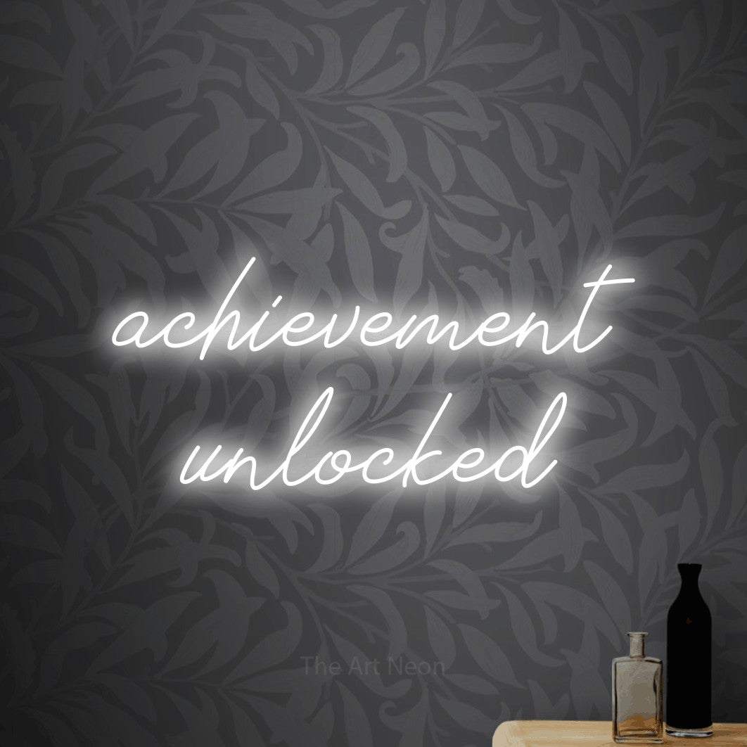 LED neon sign reading “achievement unlocked”, arranged in 2 lines.