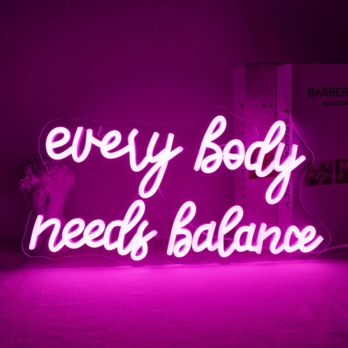 Bilden visar en levande "Every Body Needs Balance" LED-neonskylt.