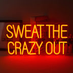 En livlig LED-neonskylt som visar frasen "Sweat The Crazy Out" i ett lekfullt kursivt teckensnitt.