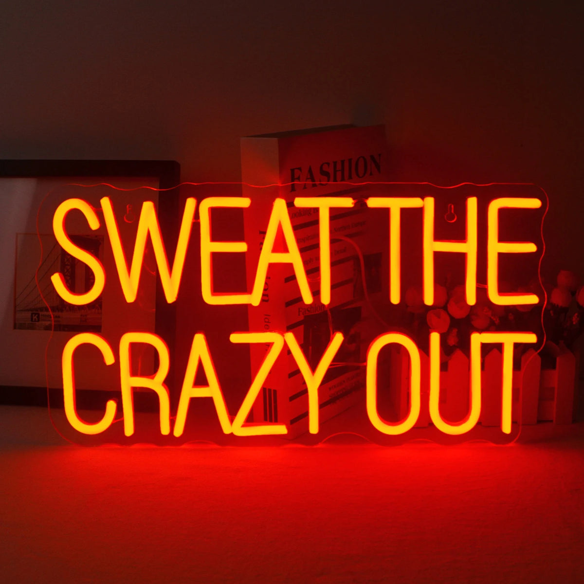 En livlig LED-neonskylt som visar frasen "Sweat The Crazy Out" i ett lekfullt kursivt teckensnitt.