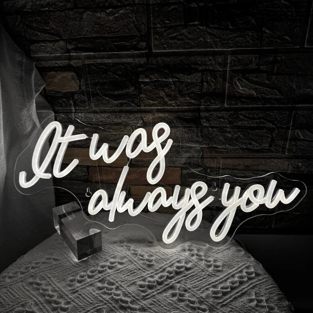 Bilden har en levande LED-neonskylt som visar orden "It Was Always You" i ett snyggt, kursivt teckensnitt.