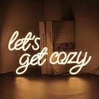 Bilden har en levande LED-neonskylt som visar frasen "Let's Get Cozy" i ett varmt, välkomnande manustypsnitt.