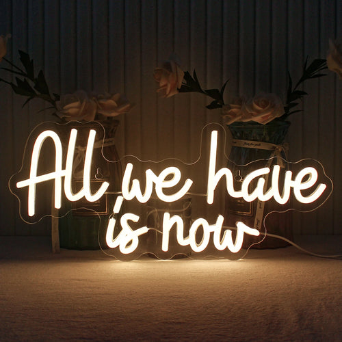 Bilden visar en handgjord LED-neonskylt med orden "All We Have Is Now" i livfulla, självlysande bokstäver.