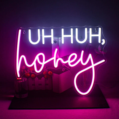 Bilden har en levande, handgjord LED-neonskylt som visar frasen "Uh Huh" i ett livligt kursivt manus.