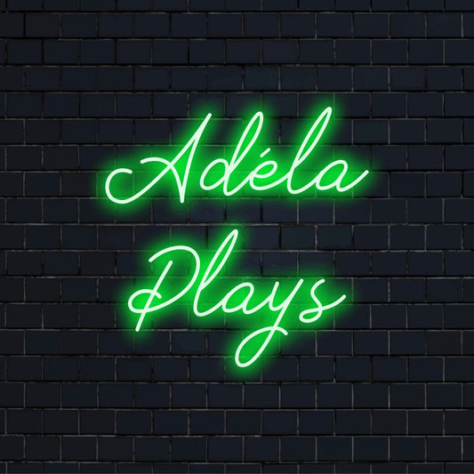 Adela Plays Custom Name Neon Sign, bright neon glow on dark brick wall
