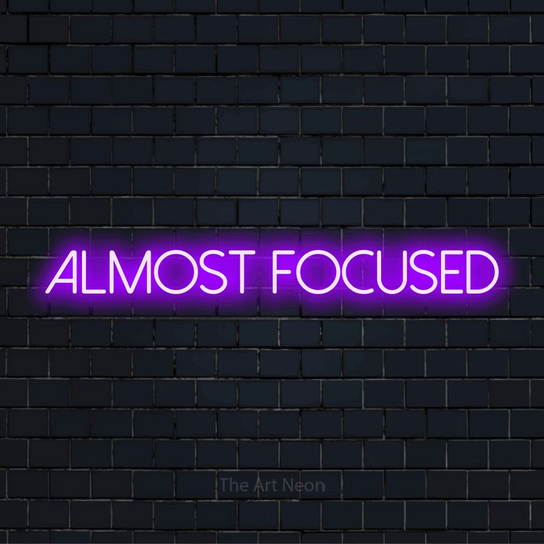 "Almost Focused" neon text design on a black brick wall