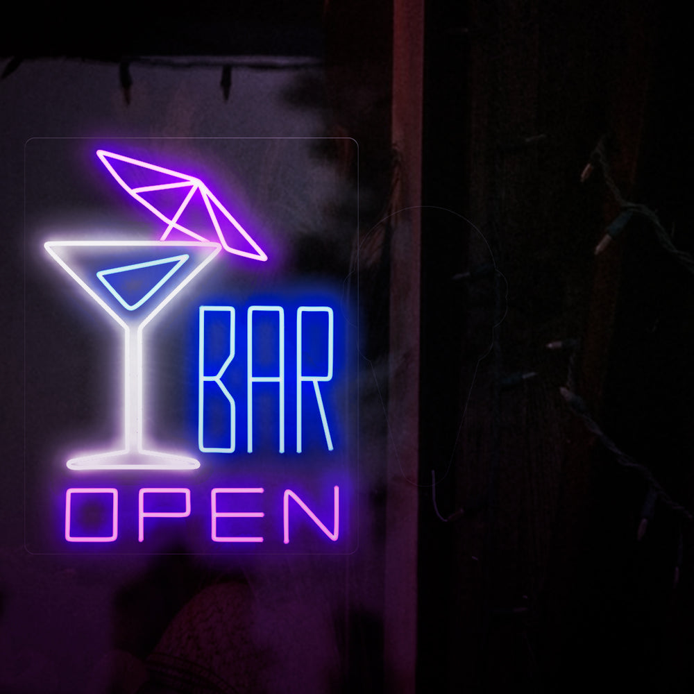 Bilden visar en neonskylt med en cocktail med ett paraply till vänster och texten "öppen bar" till höger. Denna neonskylt är idealisk för barer, både inomhus och utomhus.