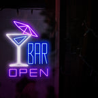 Bilden visar en neonskylt med en cocktail med ett paraply till vänster och texten "öppen bar" till höger. Denna neonskylt är idealisk för barer, både inomhus och utomhus.