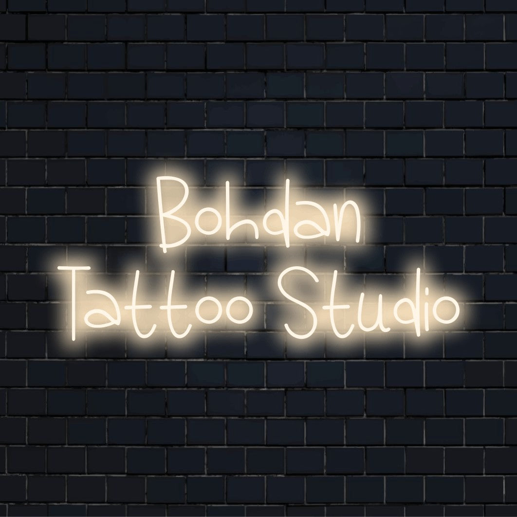 Bohdan Tattoo Studio Custom Name Neon Sign, bright neon lettering against black brick wall
