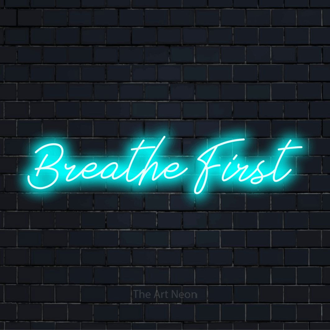 "Breathe First" script-style LED neon sign on a black brick wall
