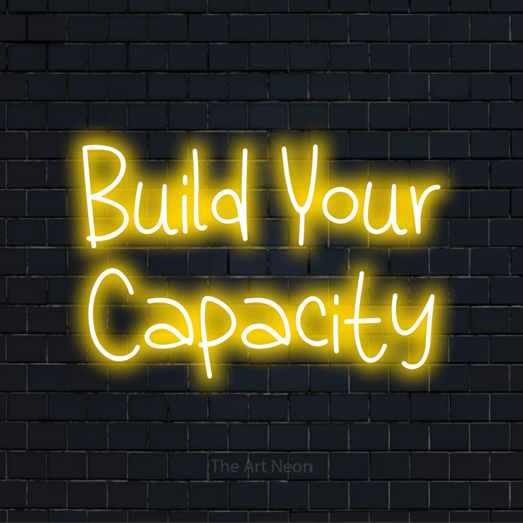 "Build Your Capacity" LED neon sign on a black brick wall