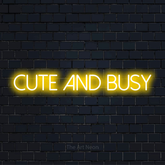 "Cute And Busy" script-style LED neon sign on a black brick wall