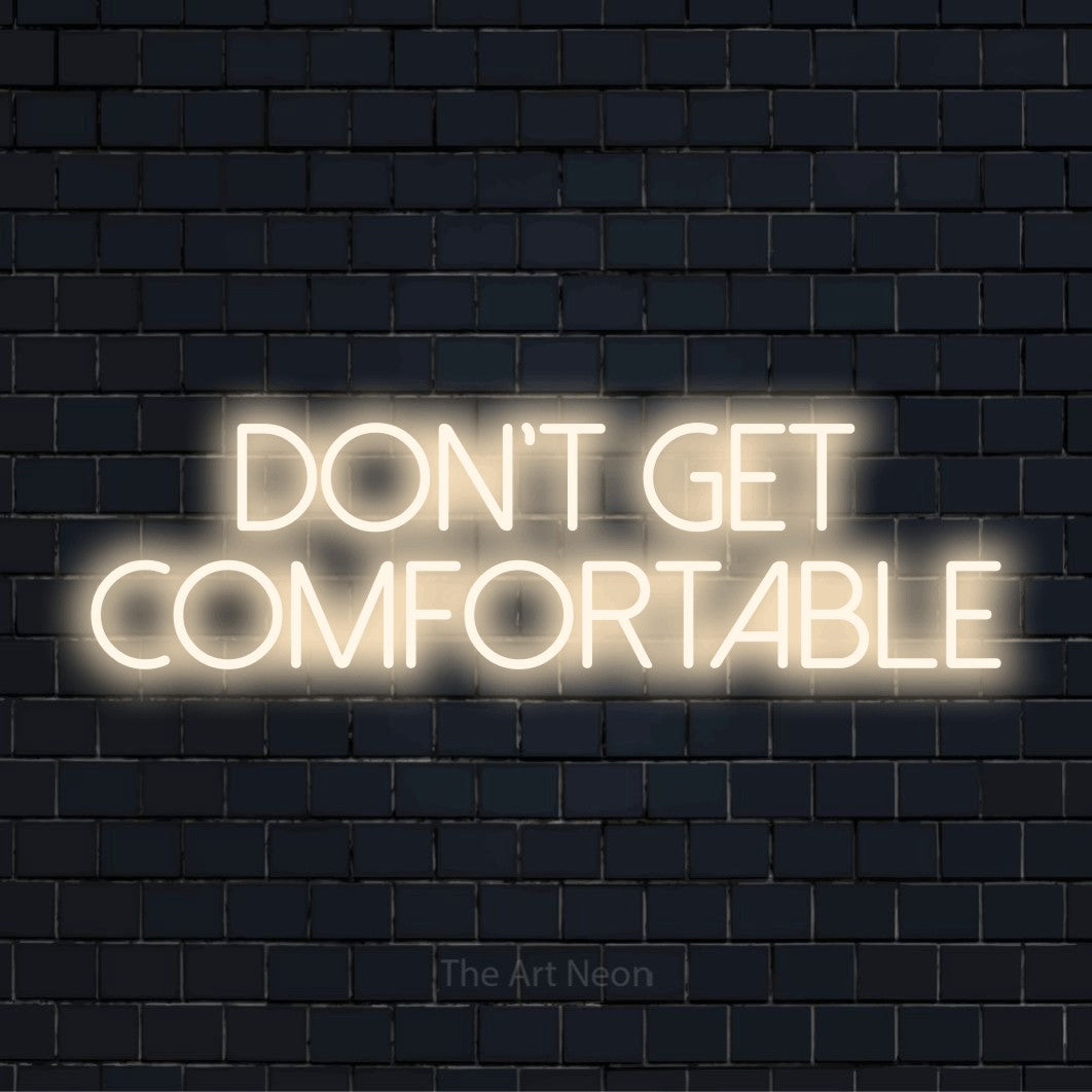 "Don’t Get Comfortable" neon text design on a black brick wall