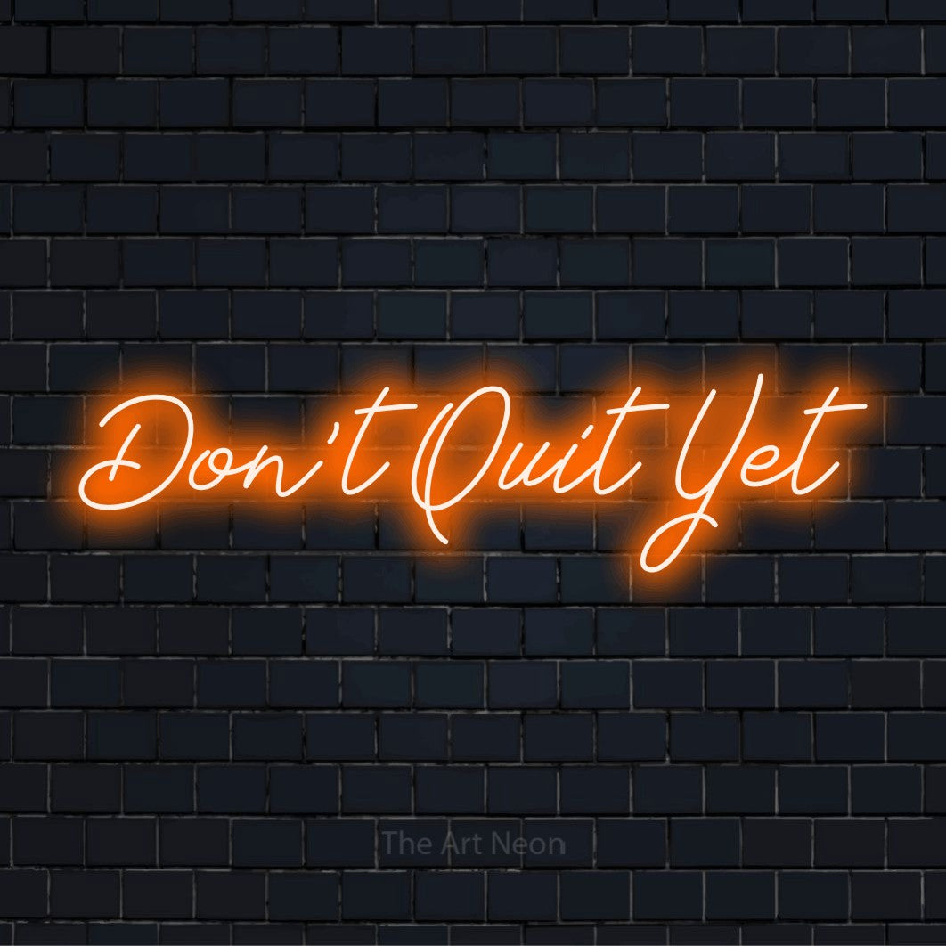 "Don’t Quit Yet" script-style LED neon sign on a black brick wall