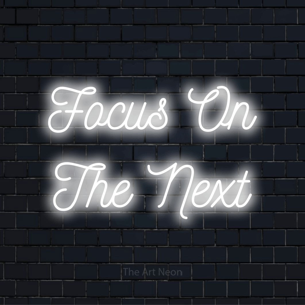 "Focus On The Next" LED neon sign on a black brick wall