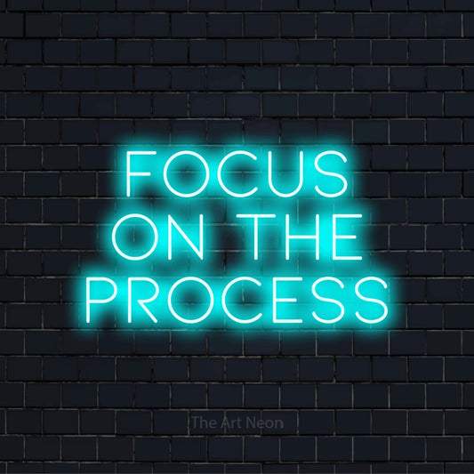 "Focus On The Process" script-style LED neon sign on a black brick wall