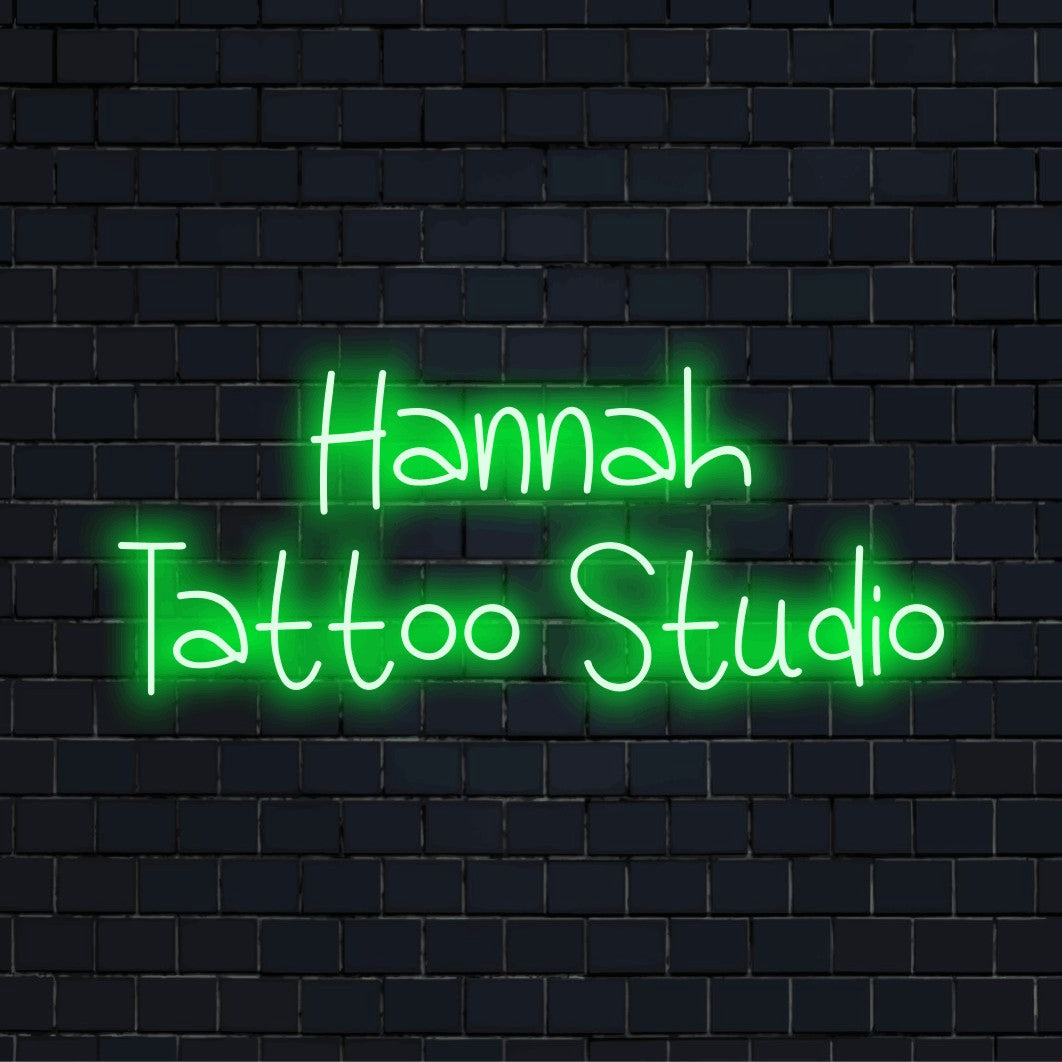 Hannah Tattoo Studio Custom Name Neon Sign, glowing lettering on dark brick wall