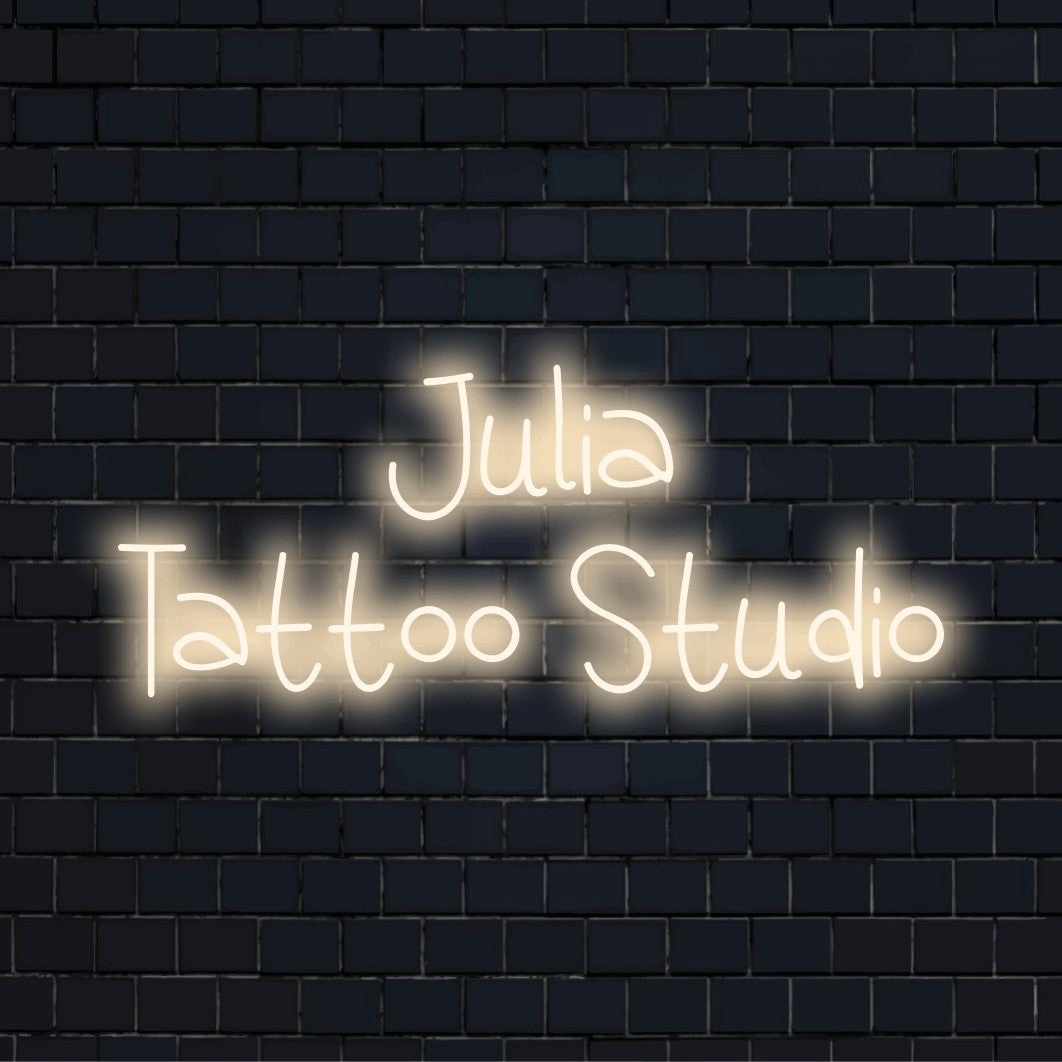 Julia Tattoo Studio Custom Name Neon Sign, glowing lettering on dark brick wall