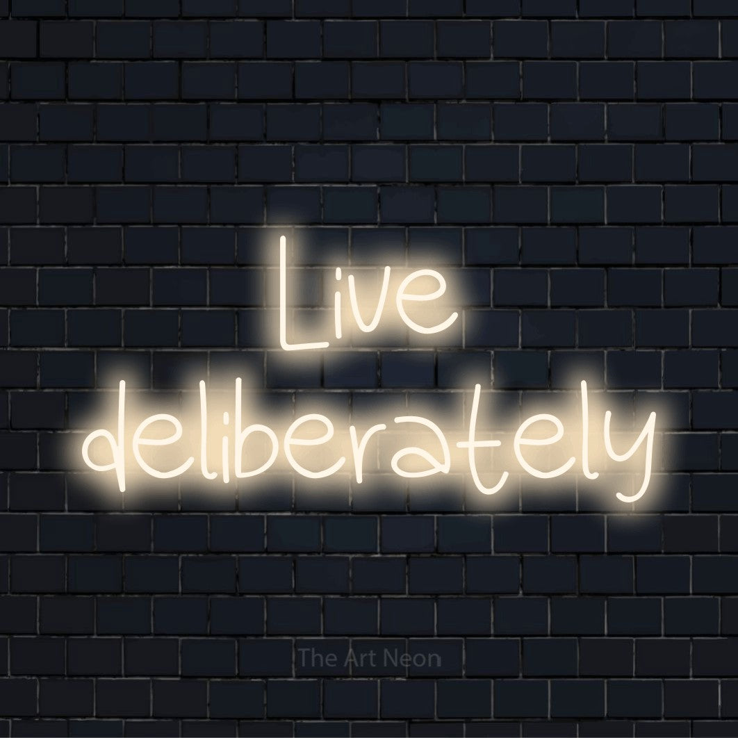 "Live Deliberately" script-style LED neon sign on a black brick wall
