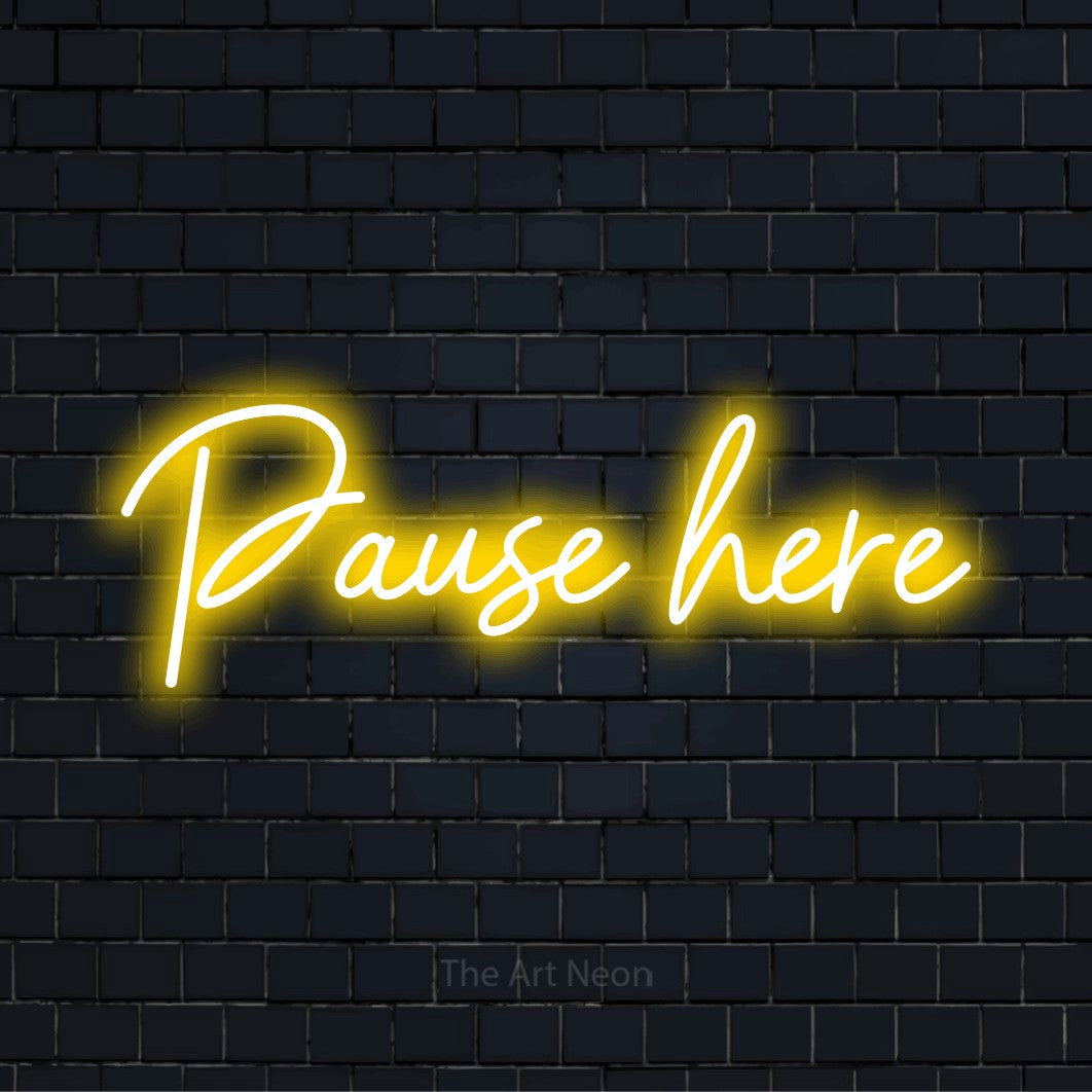 "Pause Here" LED neon sign on a black brick wall