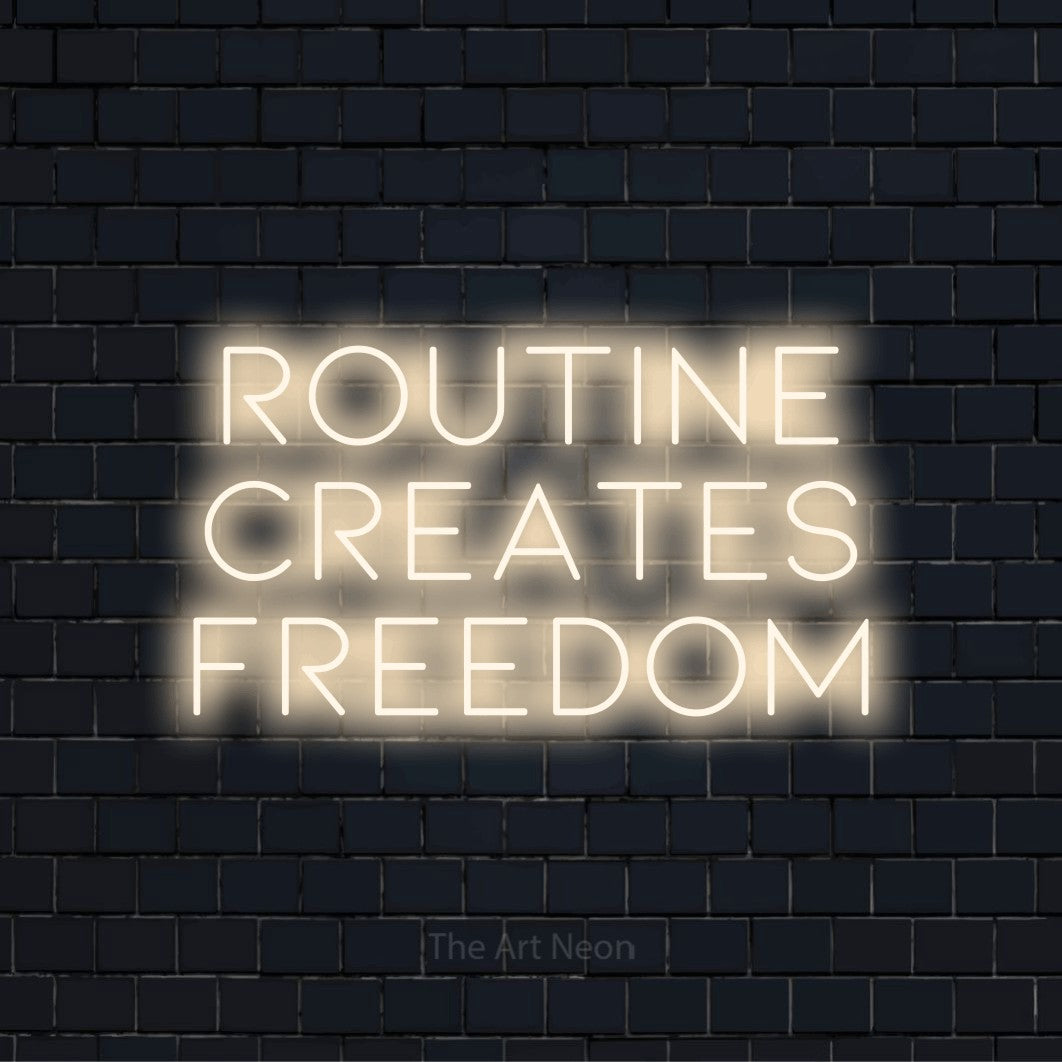 "Routine Creates Freedom" neon text design on a black brick wall