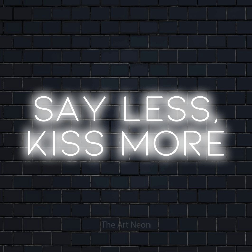 "Say Less, Kiss More" script-style LED neon sign on a black brick wall