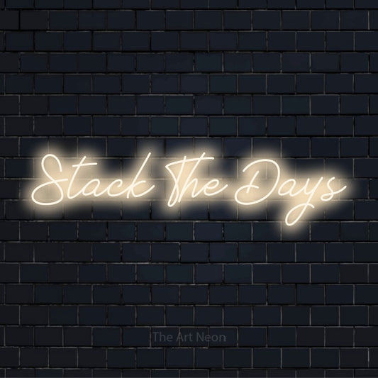 "Stack The Days" text design with neon effect on a black brick wall