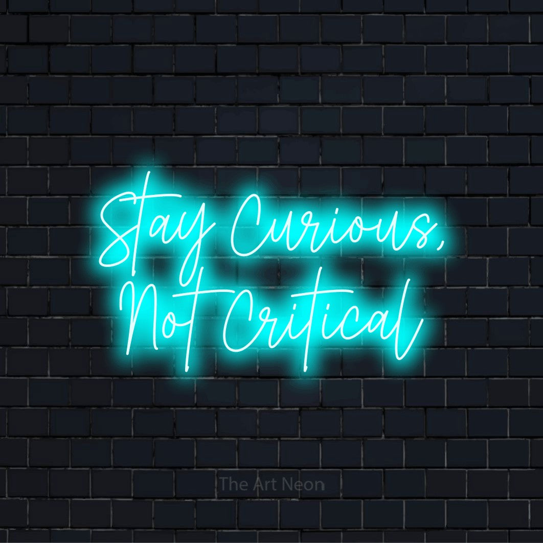 "Stay Curious, Not Critical" glowing LED neon sign on a black brick wall