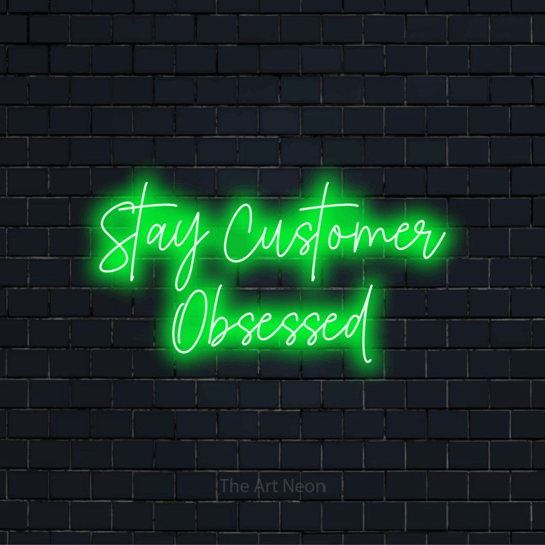 "Stay Customer Obsessed" neon text design on a black brick wall