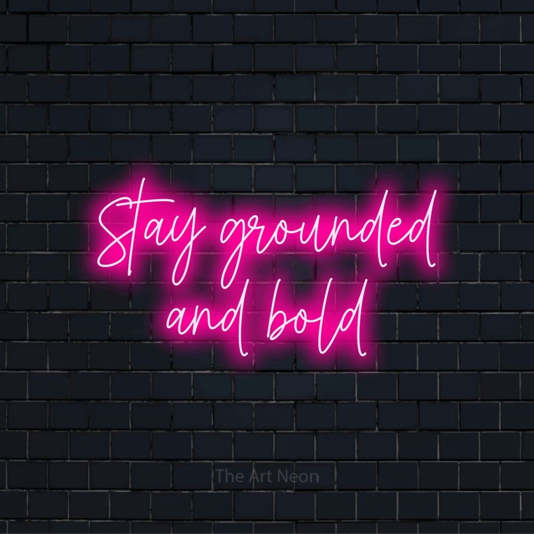 "Stay Grounded And Bold" glowing LED neon sign on a black brick wall
