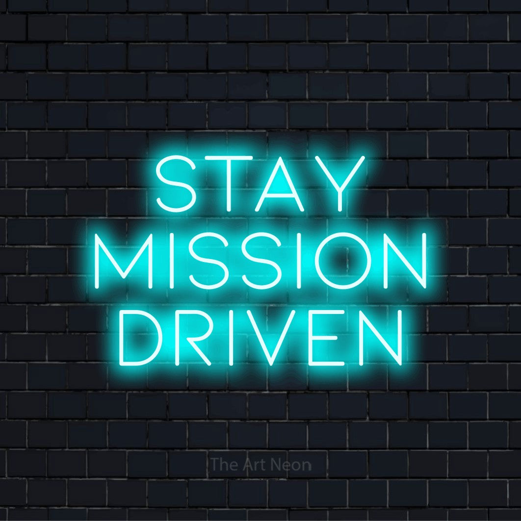 "Stay Mission Driven" script-style LED neon sign on a black brick wall
