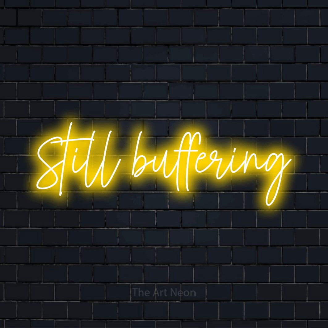 "Still Buffering" script-style LED neon sign on a black brick wall