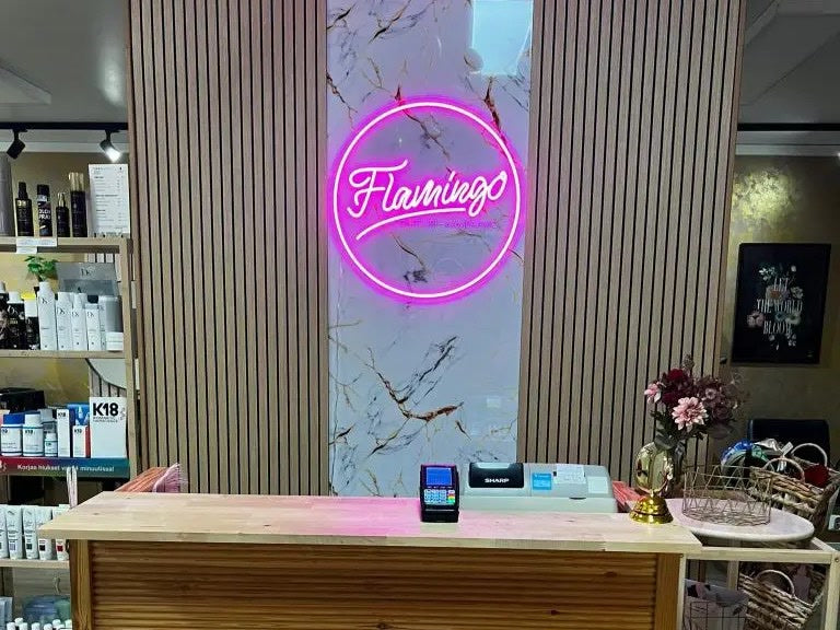 Rosa Flamingo-logotyp i neon bakom receptionsdisken hos Parturi-Kampaamo Flamingo