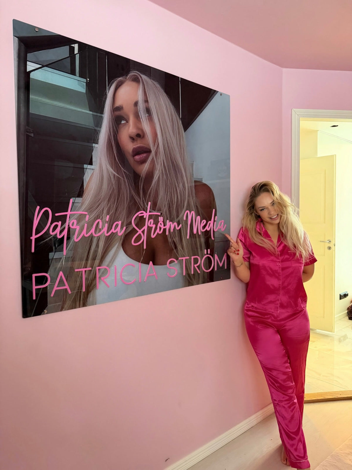 Pink Patricia Ström Media neon logo displayed beside Patricia Ström in her branded workspace