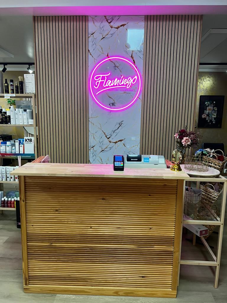 Rosa Flamingo-logotyp i neon bakom receptionsdisken hos Parturi-Kampaamo Flamingo